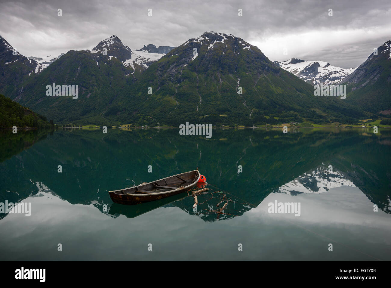 Une vieille barque dans l'eau encore de l'Oppstrynsvatnet avec reflet de la montagne dans un paysage norvégien à Hjelle. Banque D'Images