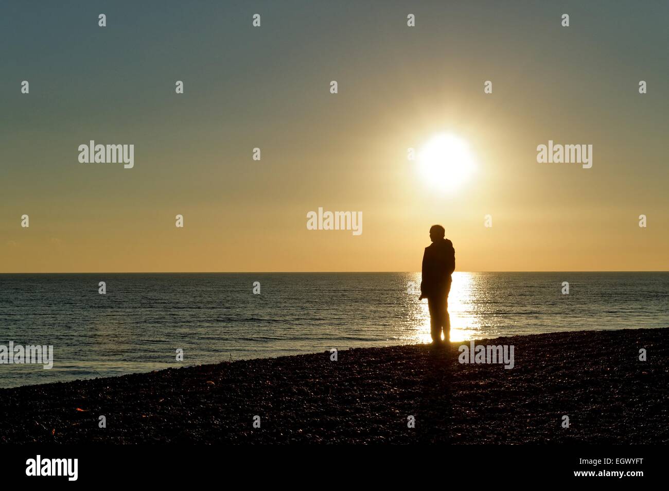 La figure masculine debout sur la plage avec le coucher du soleil derrière Banque D'Images