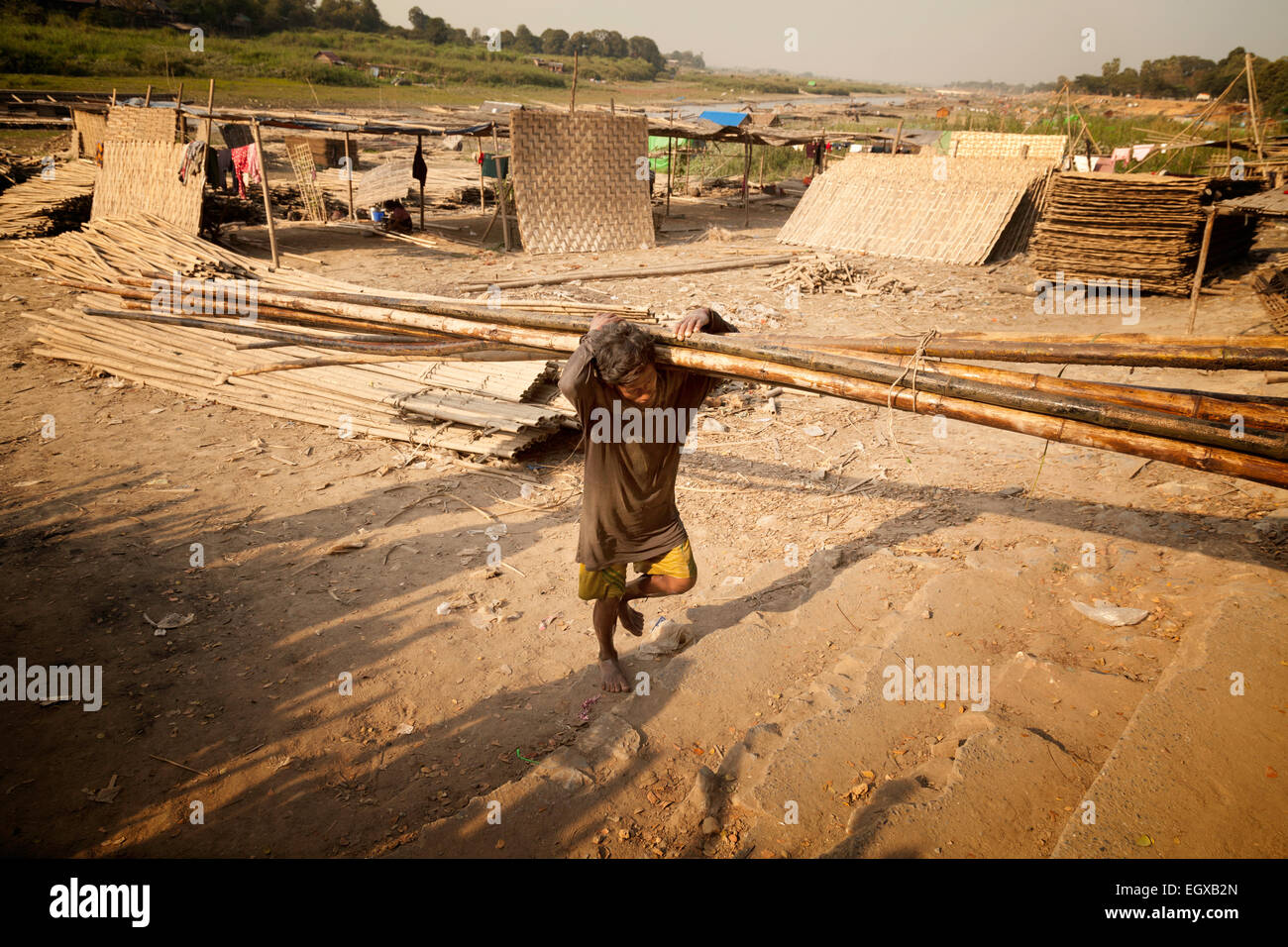 Travail manuel en Asie; Un ouvrier manuel portant des poteaux de bambou sur les rives de l'Irrawaddy (fleuve Ayeyarwady ), Mandalay, Myanmar ( birmanie ) en Asie Banque D'Images