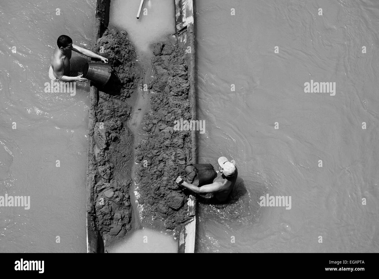 Les mineurs de sable colombien décharger seaux plein de sable dans leur bateau ancré au milieu de la rivière à Cartago, Colombie. Banque D'Images