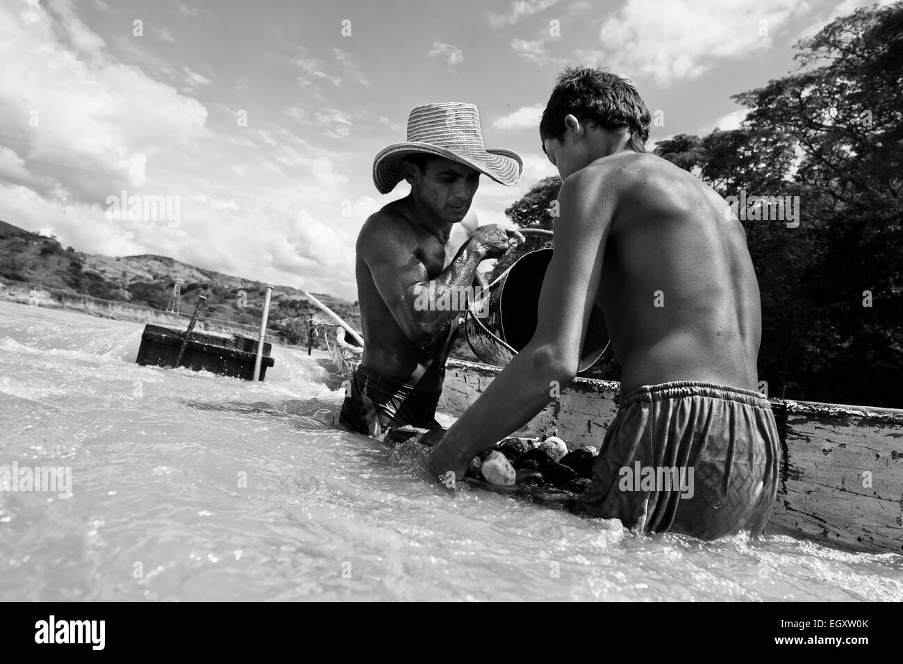 Les mineurs de sable colombien décharger un seau rempli de gravier dans leur bateau au milieu de la rivière à Cartago, Colombie. Banque D'Images