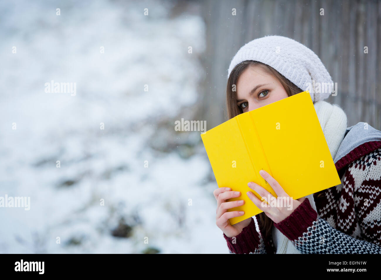 Jeune femme se cachant derrière livre jaune Banque D'Images