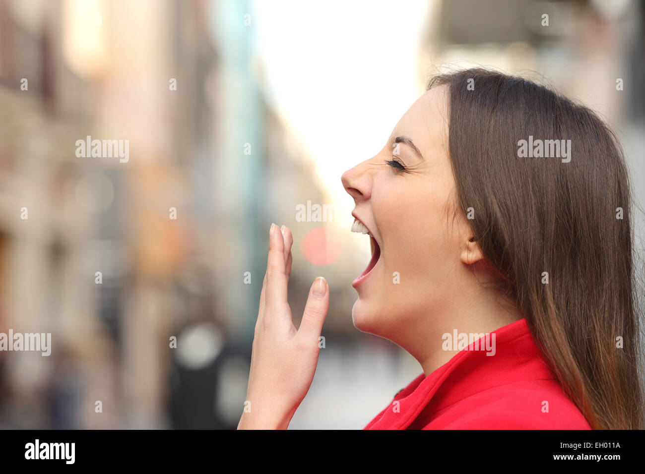 Tired woman yawning dans la rue le matin avec un flou d'arrière-plan urbain Banque D'Images