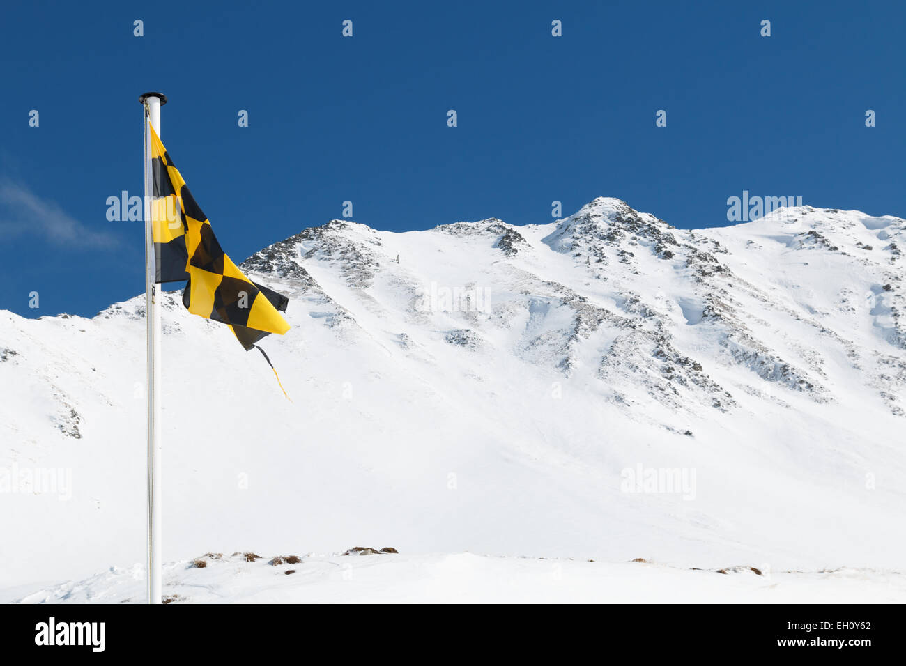 Jaune et Noir d'un indicateur d'alerte de risque d'avalanche voler contre une crête de montagne de neige. Le pavillon présente un risque élevé d'avalanche. Banque D'Images