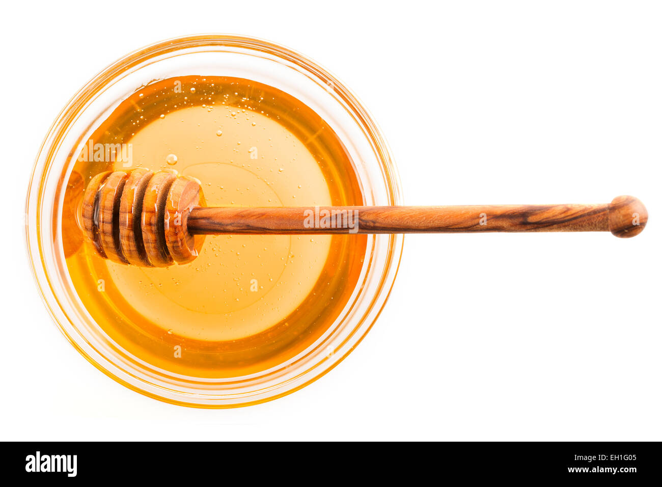 Le miel dans un bol en verre avec un pendage stick, isolé sur blanc. Banque D'Images