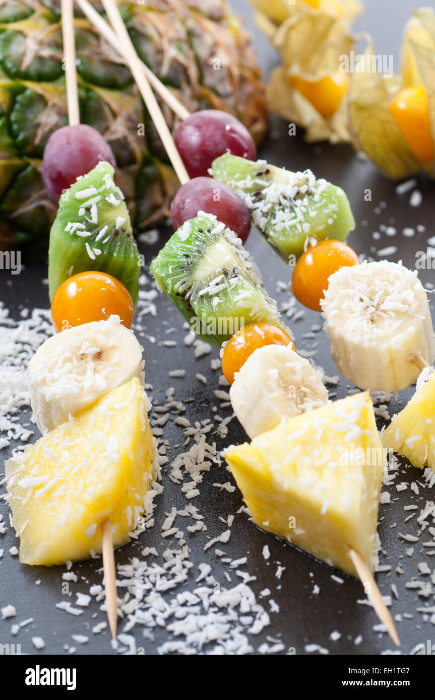 Brochettes à l'ananas, banane, cerise d'hiver, kiwi et raisin. Noix de coco desséchée sur le dessus. Banque D'Images