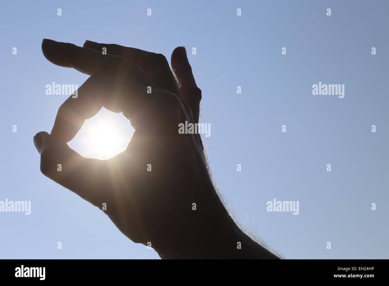 La main d'un homme rendant le symbole OK autour du soleil sur un fond de ciel bleu au-dessus de lui Banque D'Images