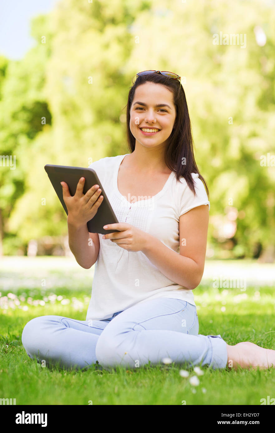 Smiling young girl with tablet pc sitting on grass Banque D'Images