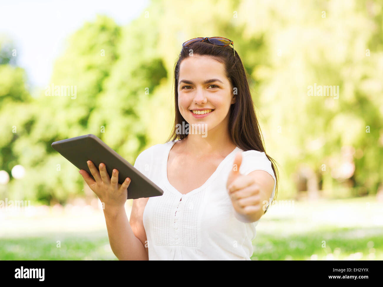 Smiling young girl with tablet pc sitting on grass Banque D'Images