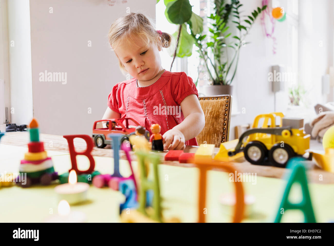 3 ans, fille, dans une robe rouge joue avec des jouets pour son anniversaire à la table, Allemagne Banque D'Images
