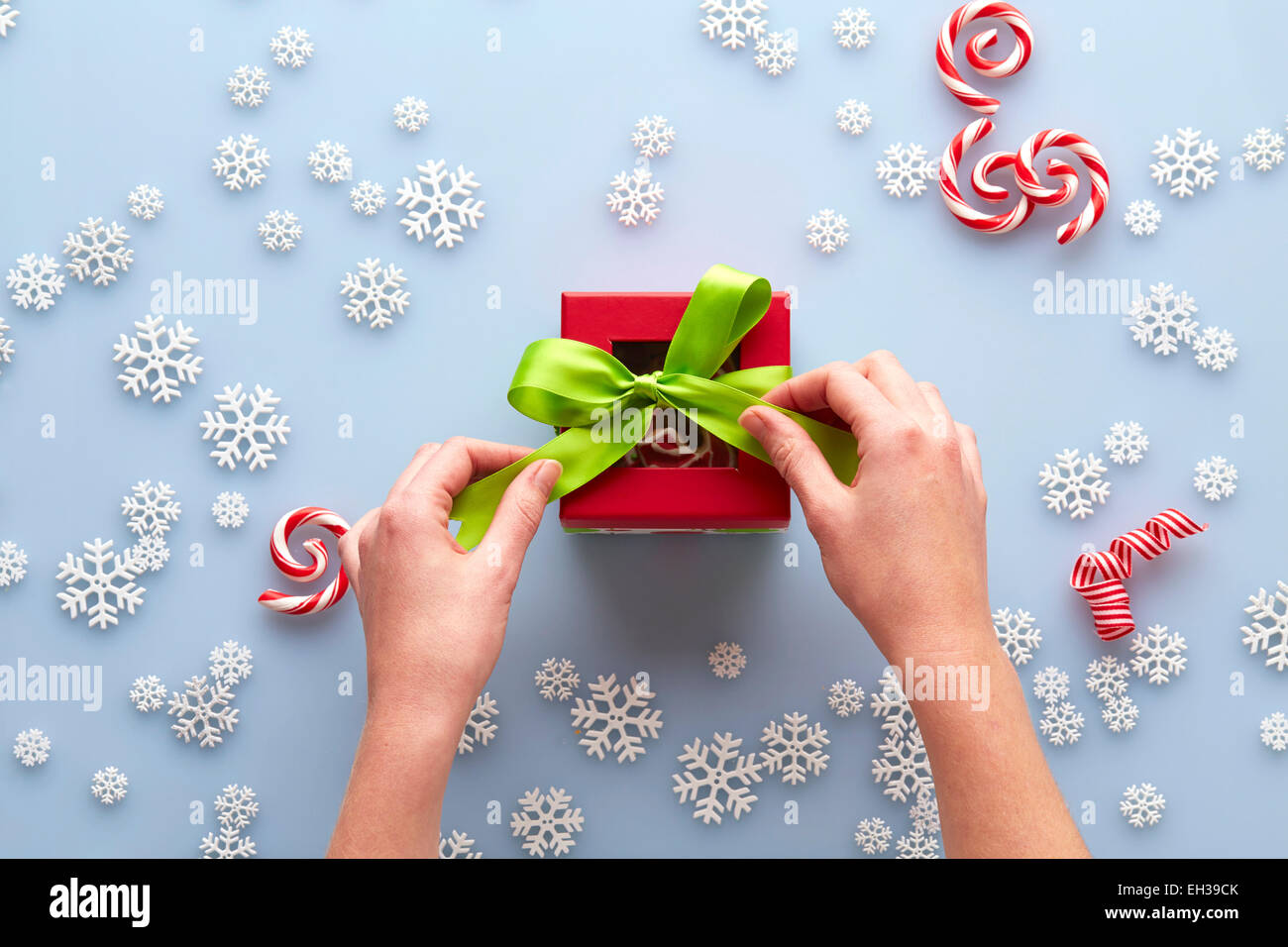 Vue de dessus de mains Lier Noeud sur présent avec des flocons et Candy Cane Swirls, Studio Shot Banque D'Images