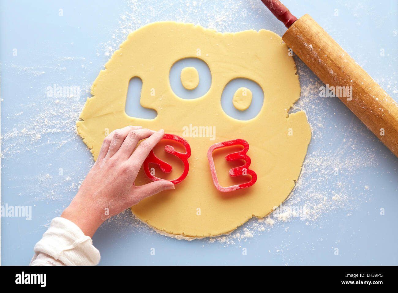 Vue de dessus de la main de femme à l'aide d'un emporte-pièce pour épeler lâche dans la pâte à biscuit roulé hors Suger, Studio Shot Banque D'Images