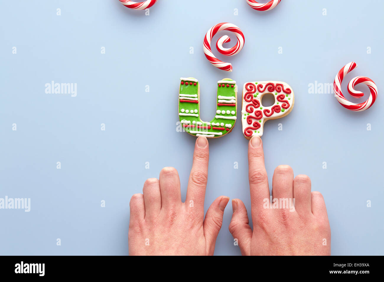 Vue de dessus de Woman's Hands et biscuits de Noël en sucre l'orthographe sur fond bleu avec des tourbillons de canne Banque D'Images