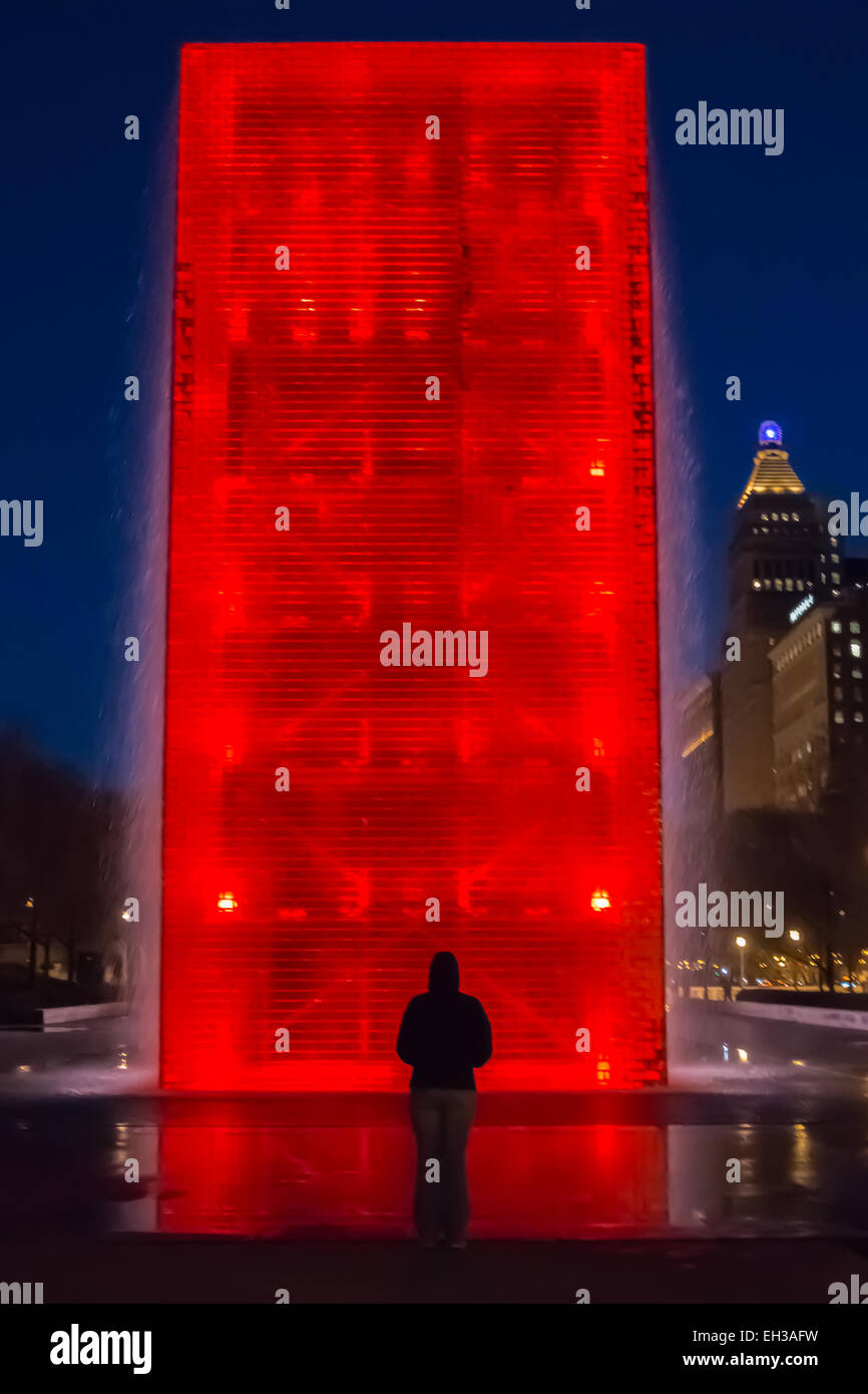 Une femme s'arrête en face d'une fontaine qui coule avec éclairage LED rouge allumée Banque D'Images