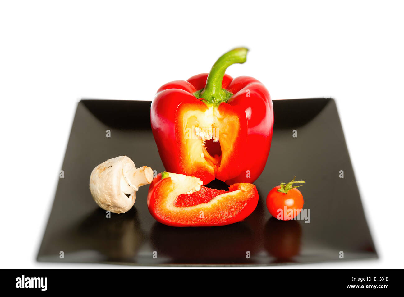 Poivron rouge, tomates et champignons sur une plaque noire isolé sur fond blanc Banque D'Images