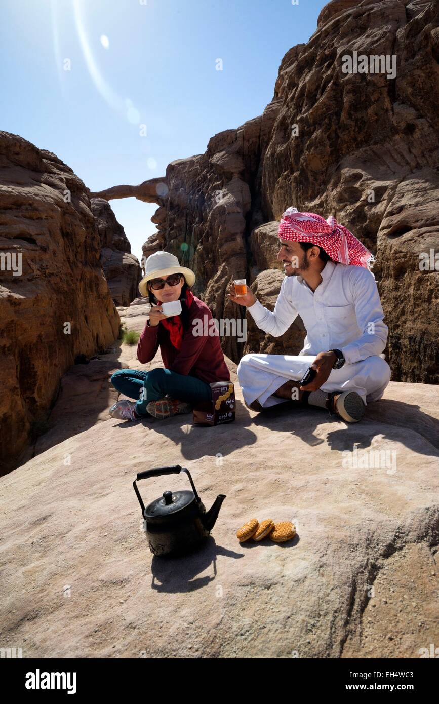 La Jordanie, Wadi Rum, zone protégée inscrite au Patrimoine Mondial de l'UNESCO, pause thé, touristique et local guide bédouin, Burdah rock bridge en arrière-plan Banque D'Images