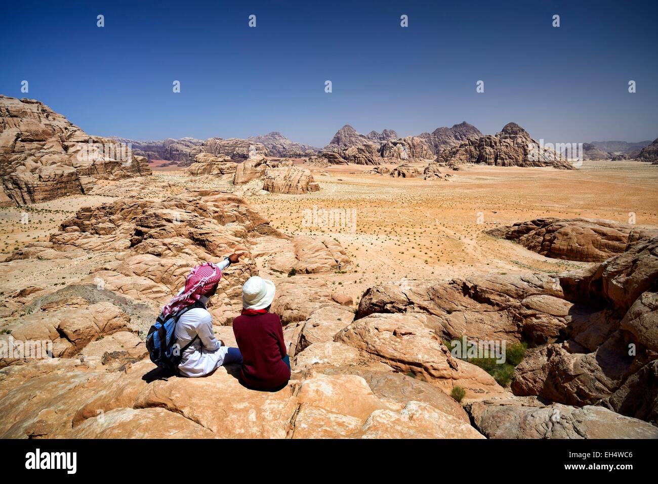 La Jordanie, Wadi Rum, zone protégée inscrite au Patrimoine Mondial de l'UNESCO, touristique et local guide bédouin assis sur un rocher, contemplant le paysage du mont Jebel Burdah Banque D'Images