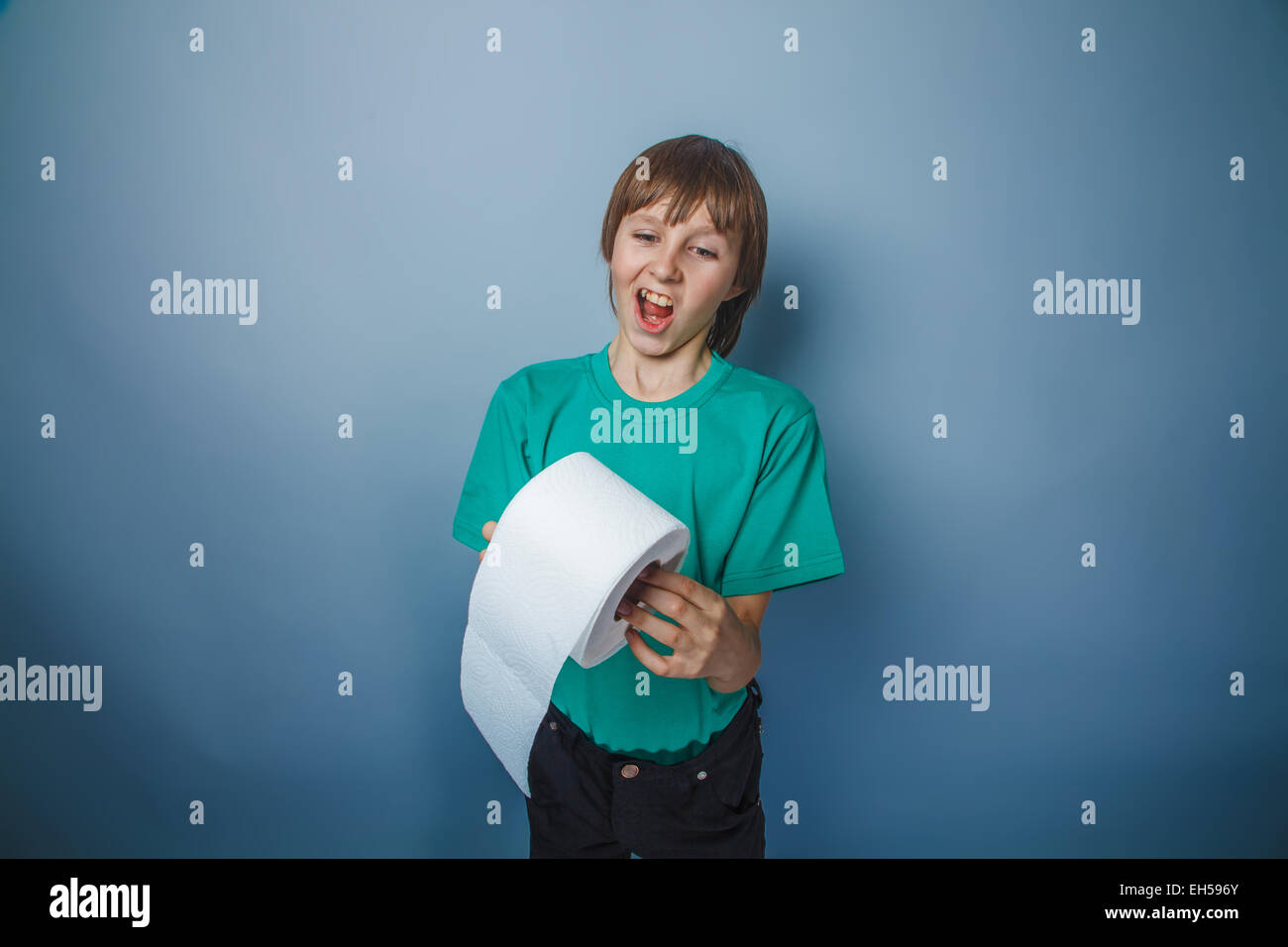 L'apparence de l'adolescent garçon en t-shirt vert tenant un papier de toilette sur un fond gris Banque D'Images