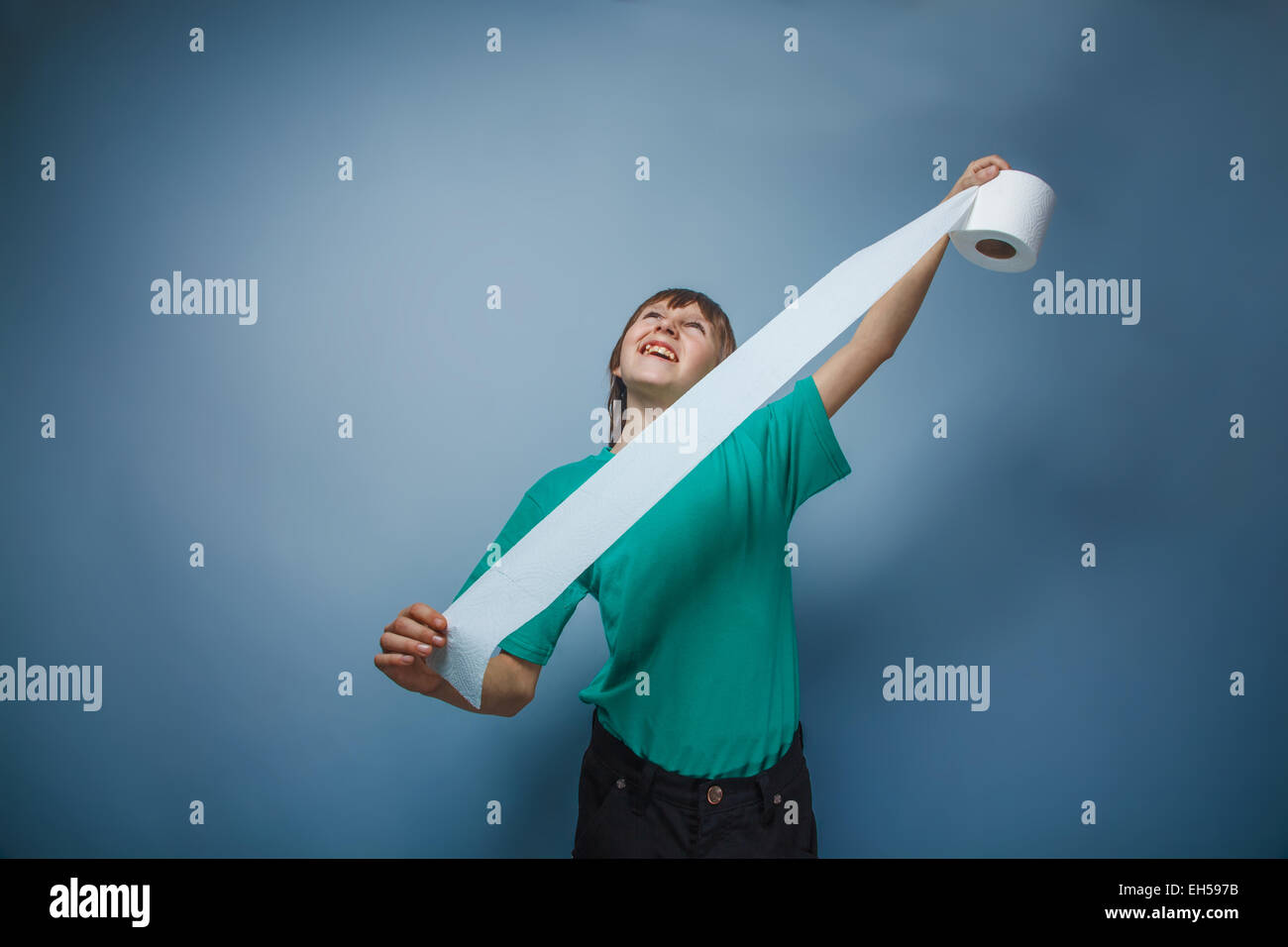 L'apparence de l'adolescent garçon dans une chemise verte holding dénoué papier de toilette sur un fond gris, méfait Banque D'Images