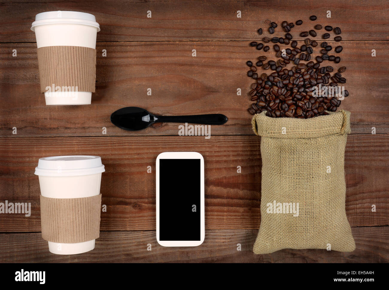 High angle shot de tasses à café à emporter et un sac de toile avec des haricots tomber sur une table en bois rustique. Un téléphone cellulaire et cuillère Banque D'Images