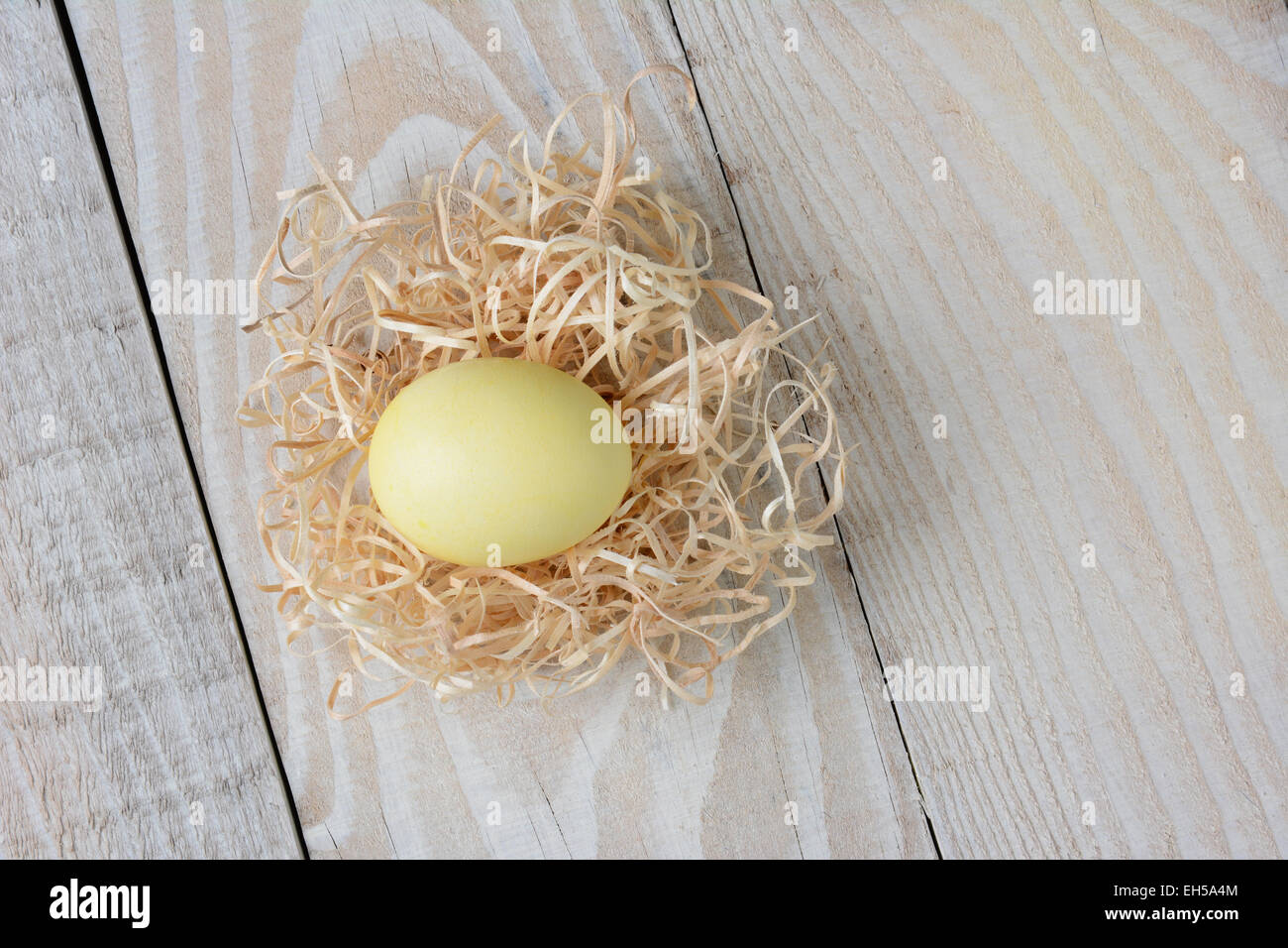 Passage tiré d'un teint jaune d'oeufs de Pâques dans un nid fait de raphia sur un cadre rustique en bois blanc table de cuisine. Format horizontal. Banque D'Images