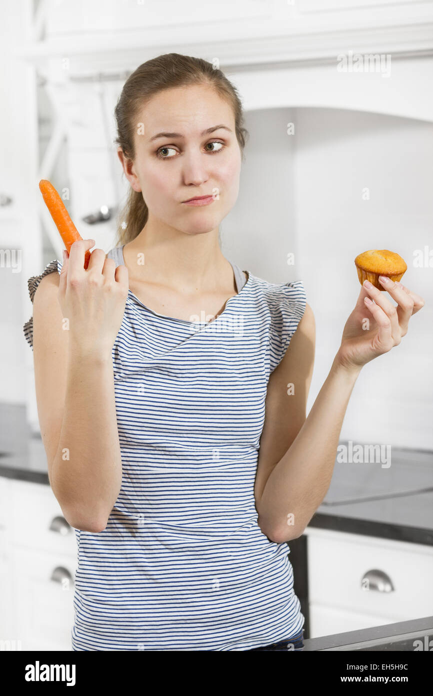 Une femme doit choisir entre l'un des muffins et une carotte. Consept de régime. Banque D'Images