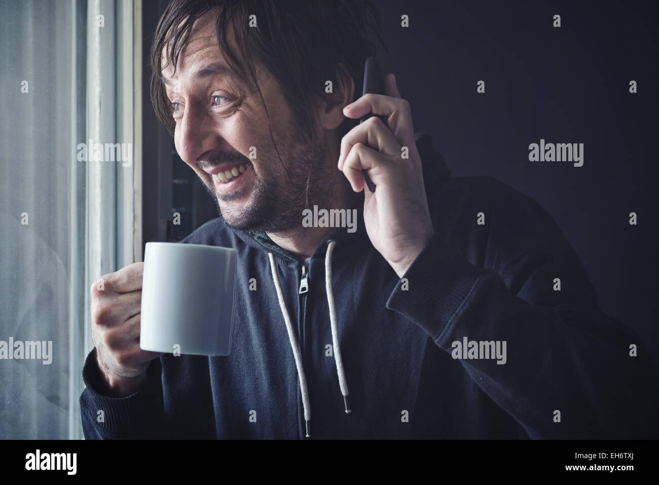 Heureux heureux homme adulte de boire du café et Talking on Mobile Phone in matin par la fenêtre. Focus sélectif avec une faible profondeur Banque D'Images