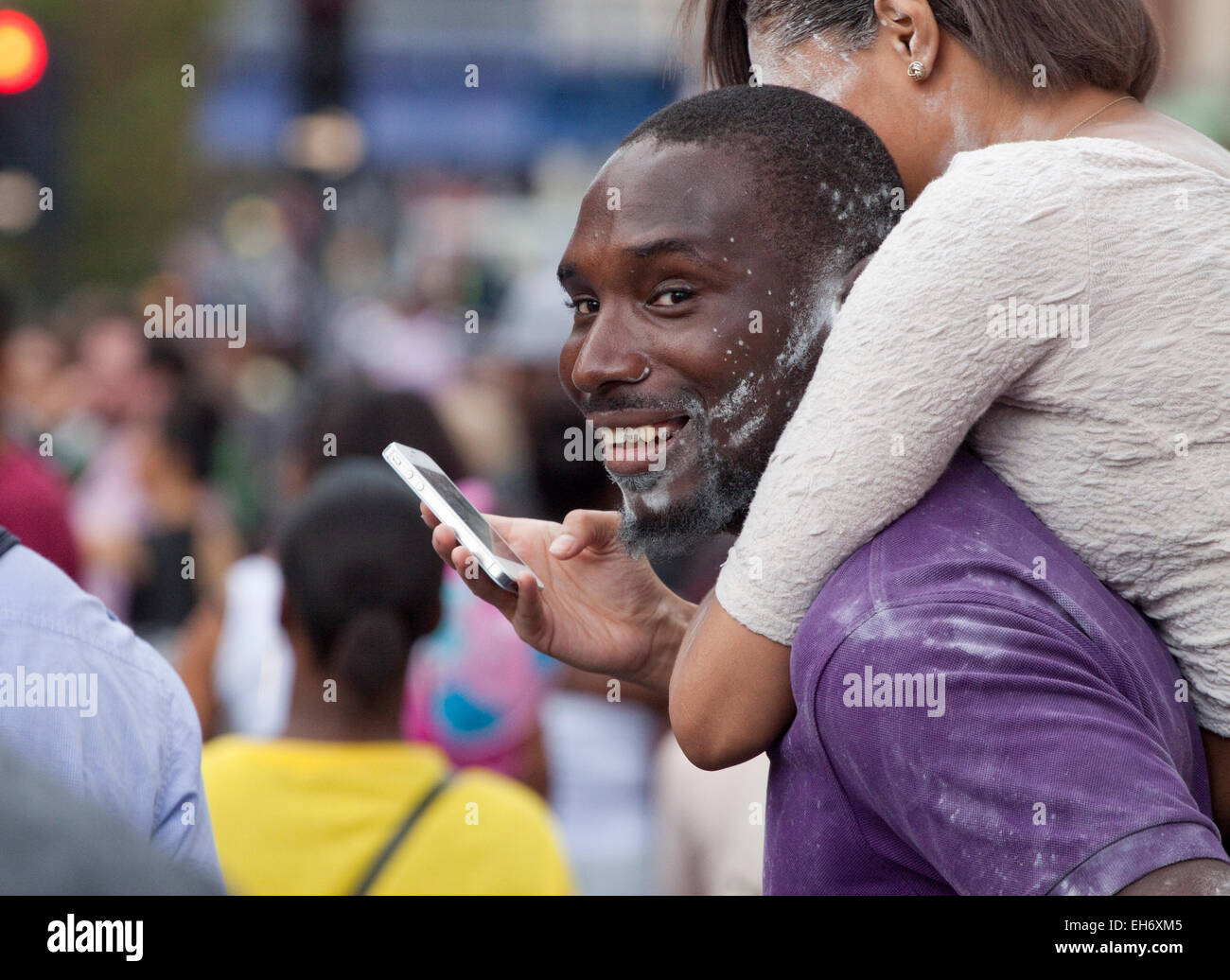 Jeune homme Afro Antillais avec sa petite amie piggy back et les deux 'splashed' avec le blanc de la poudre de talc. Banque D'Images