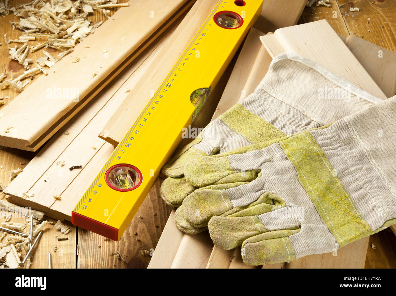Niveau des charpentiers, des clous et des gants de travail sont sur une des planches de bois Banque D'Images