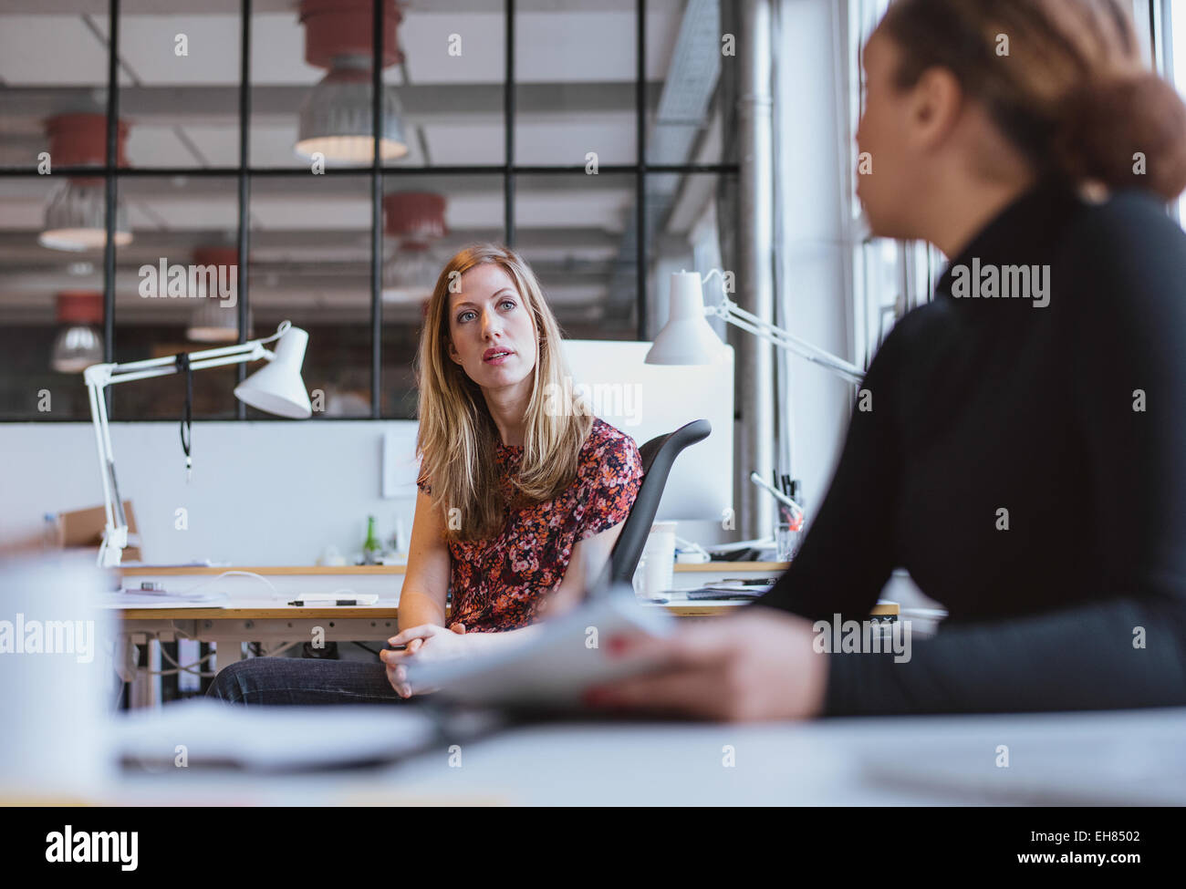 femme d'affaires parlant avec son collègue au bureau. Jeune femme assise à son bureau discutant du travail avec un collègue. Banque D'Images