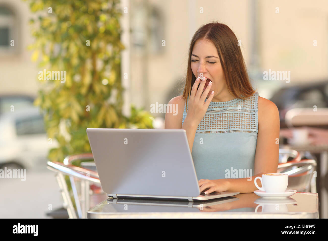 Tired woman yawning et travailler avec un ordinateur portable dans un restaurant pendant le petit déjeuner Banque D'Images