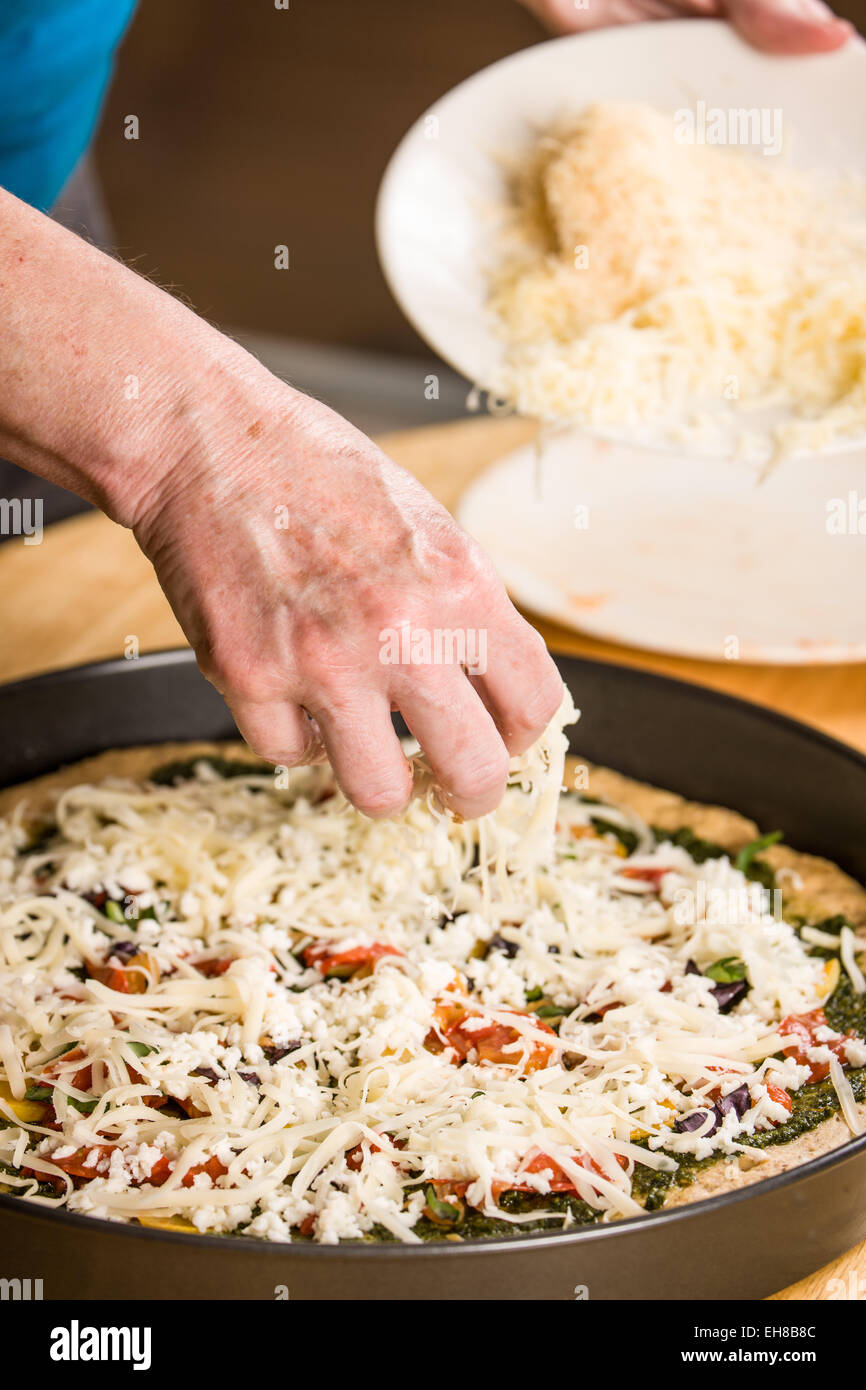 Arrosage femme suisse râpé sur une végétarienne tarte multi-grain, des pizzas à pâte épaisse Banque D'Images