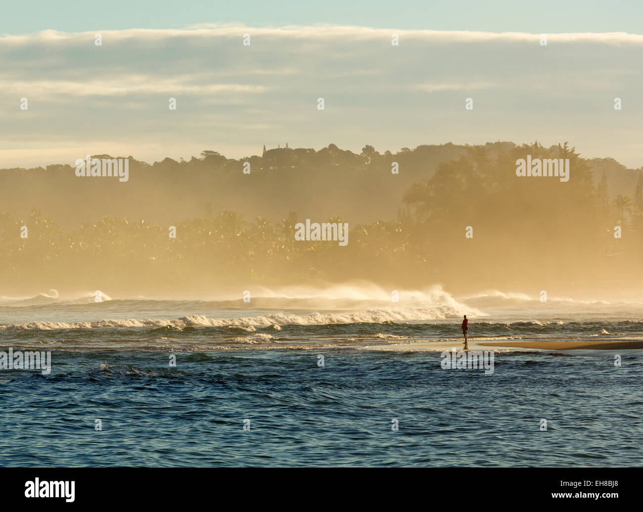 Plage à Kauai à Hanelei Bay, Hawaï - avec l'homme debout regardant les vagues et pulvérisant à l'aube Banque D'Images