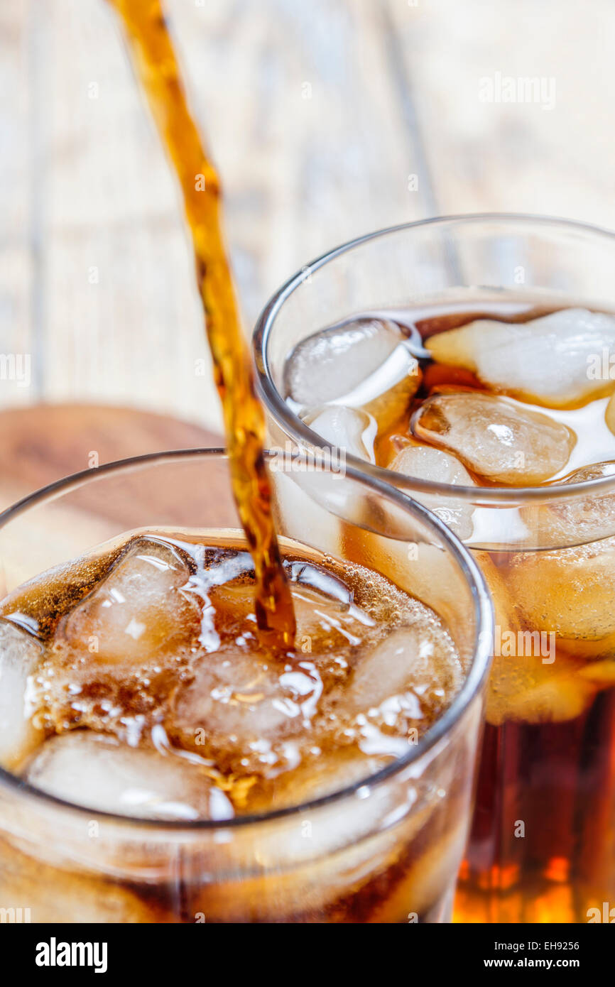 Cola et verser dans un verre avec des glaçons avec un verre d'autres déjà rempli sur table en bois rustique Banque D'Images