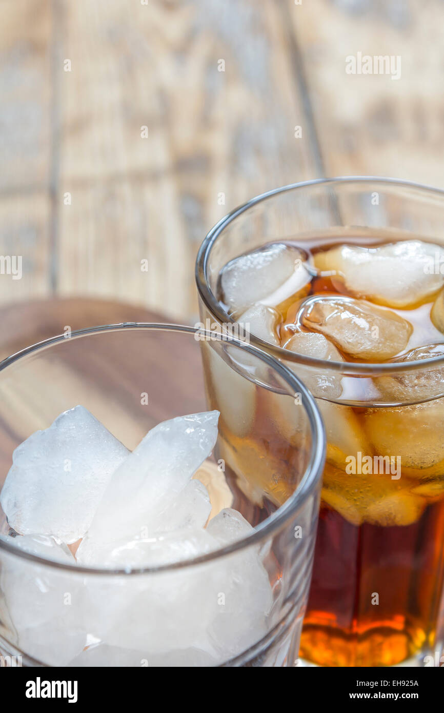 Un verre de coca et un verre vide avec des cubes de glace sur une table en bois rustique Banque D'Images