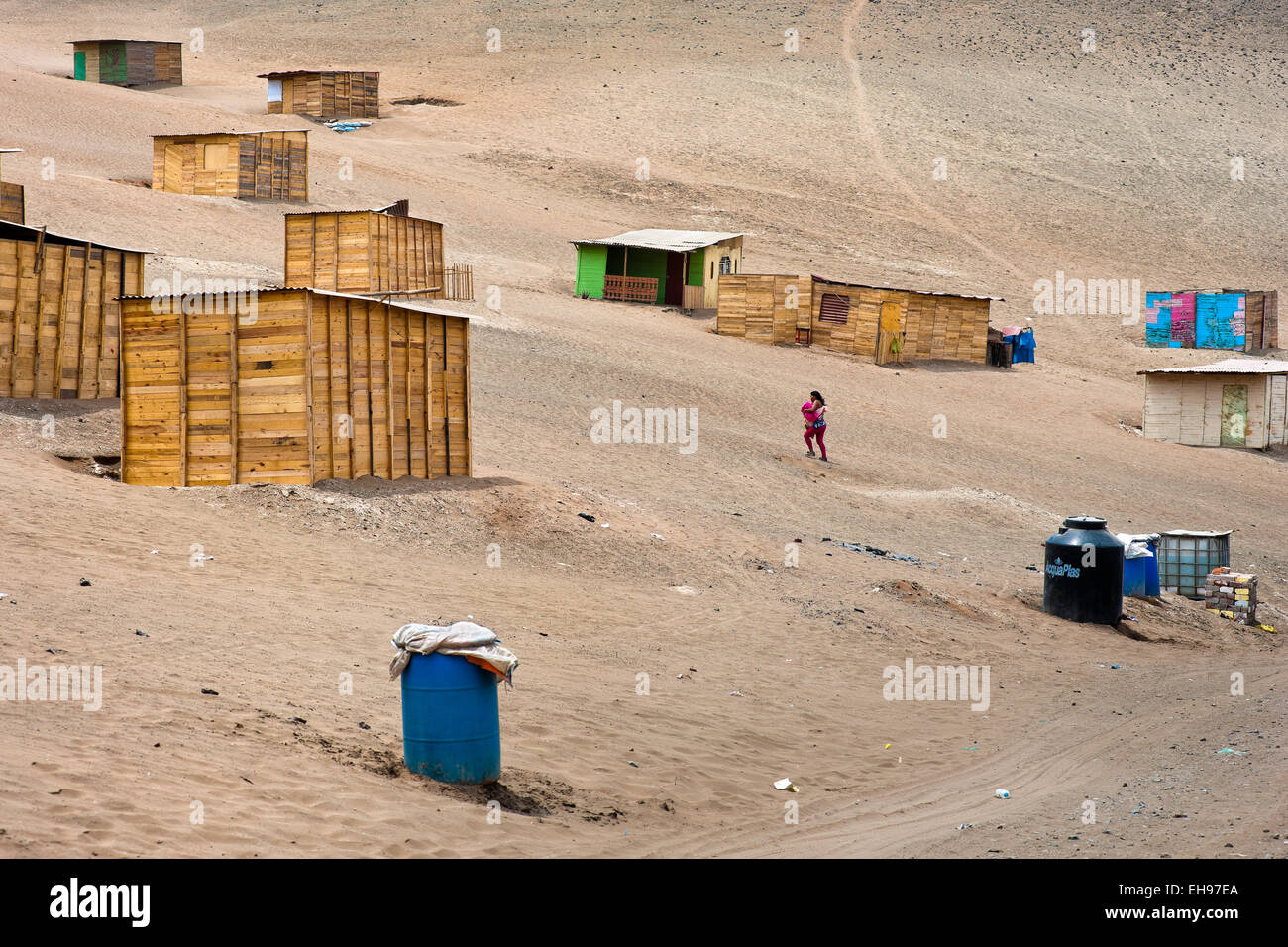 Une jeune mère porte son bébé péruvien le long de maisons en bois sur la colline de Pachacútec poussiéreux, un désert, banlieue de Lima, au Pérou. Banque D'Images