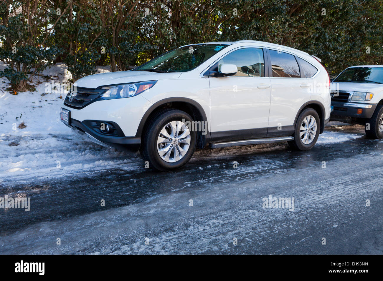 Voitures garées sur le côté de la route avec la glace noire sur la surface de la route - USA Banque D'Images