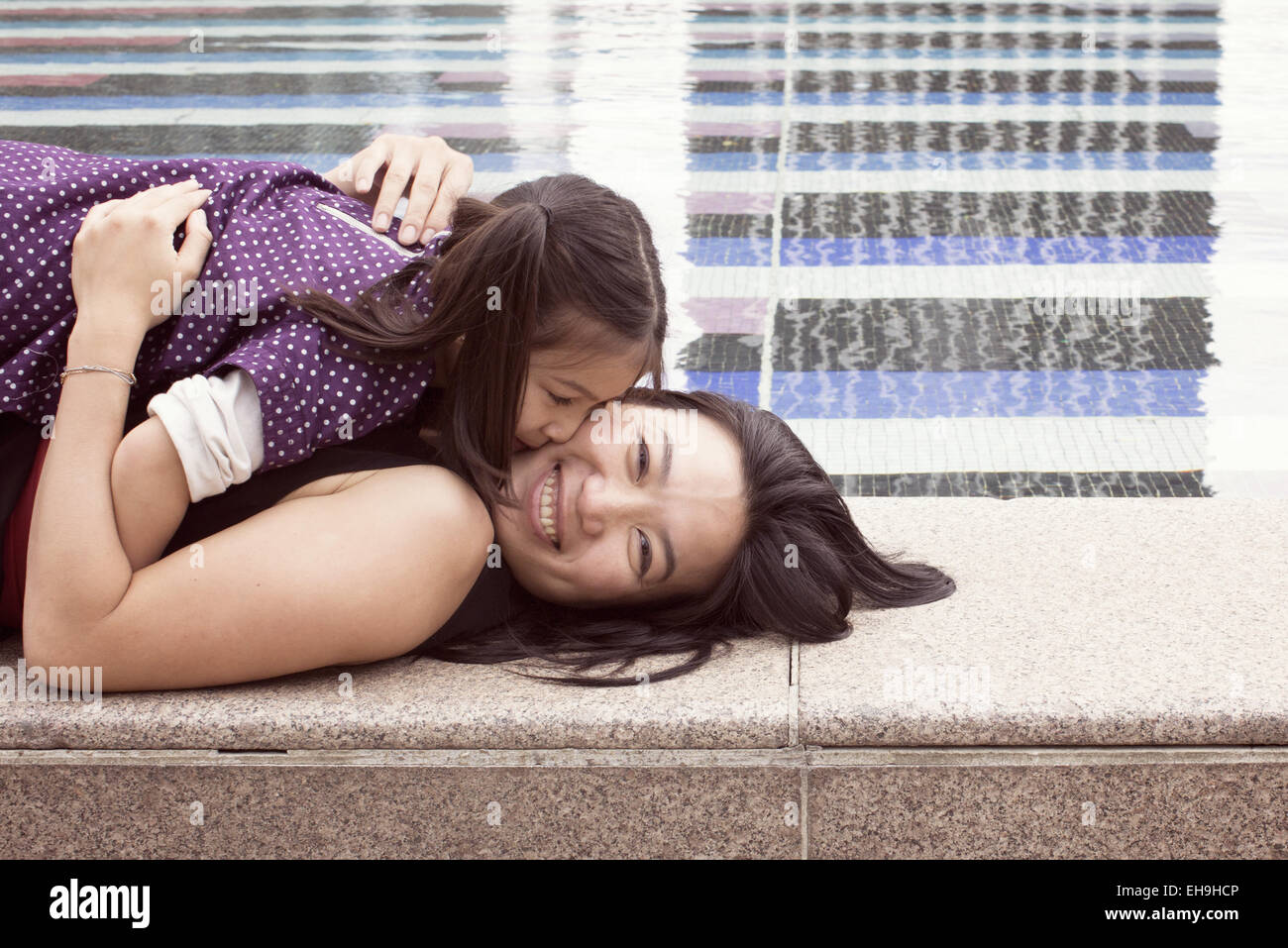 Mère et fille couché ensemble au bord de la fontaine, girl kissing woman's cheek Banque D'Images