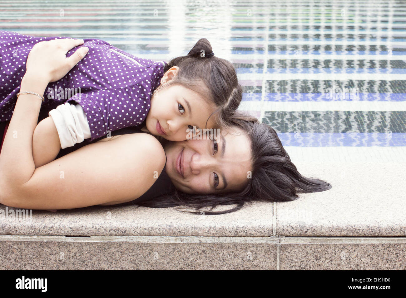Mère et fille couché ensemble sur bordure de fontaine, portrait Banque D'Images