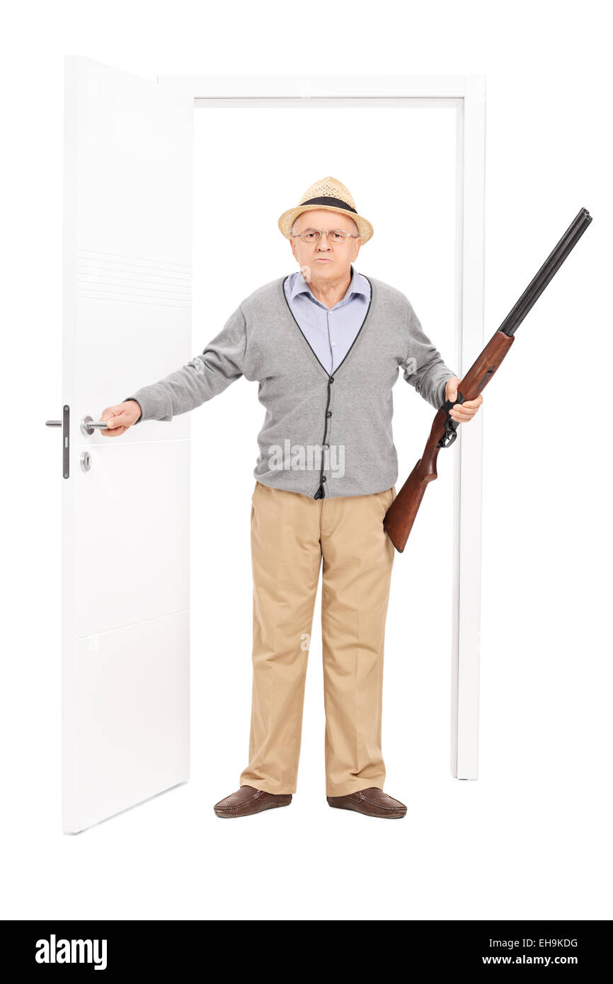 Portrait d'un senior en colère tenant un fusil de chasse et la marche à travers une porte isolé sur fond blanc Banque D'Images