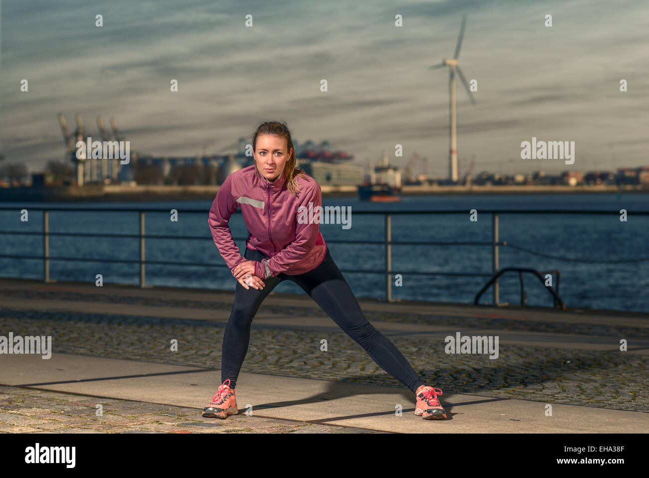 Jeune femme exerçant au bord de l'article sur l'esplanade en face du port l'échauffement des muscles stretching Banque D'Images