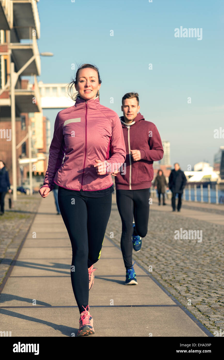 Jeune couple actif s'exécutant sur une promenade de front avec l'athletic woman ouvre la voie près de l'appareil photo Banque D'Images