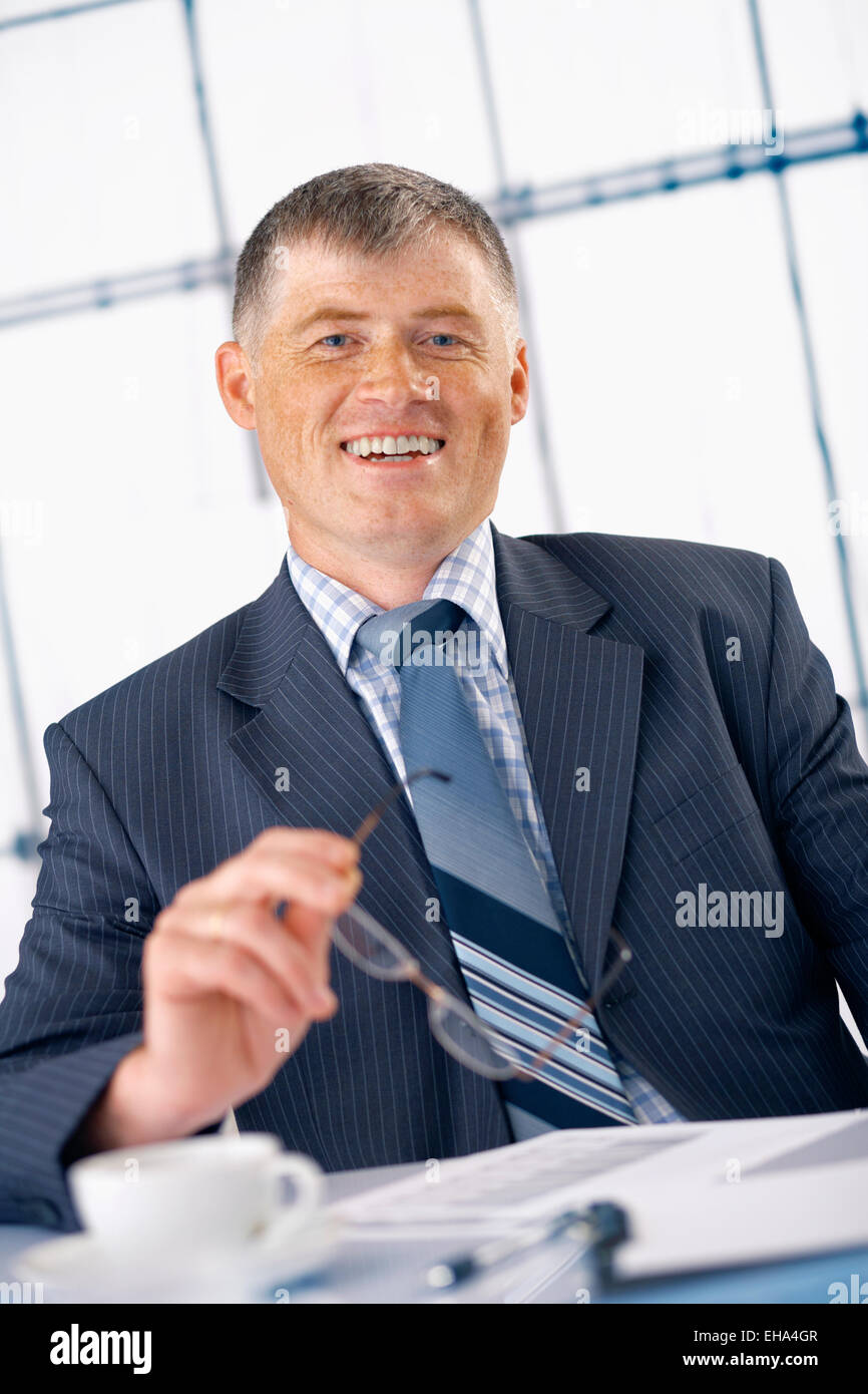 Ancien responsable d'entreprise smiling, lunettes dans sa main dans le bureau. Banque D'Images