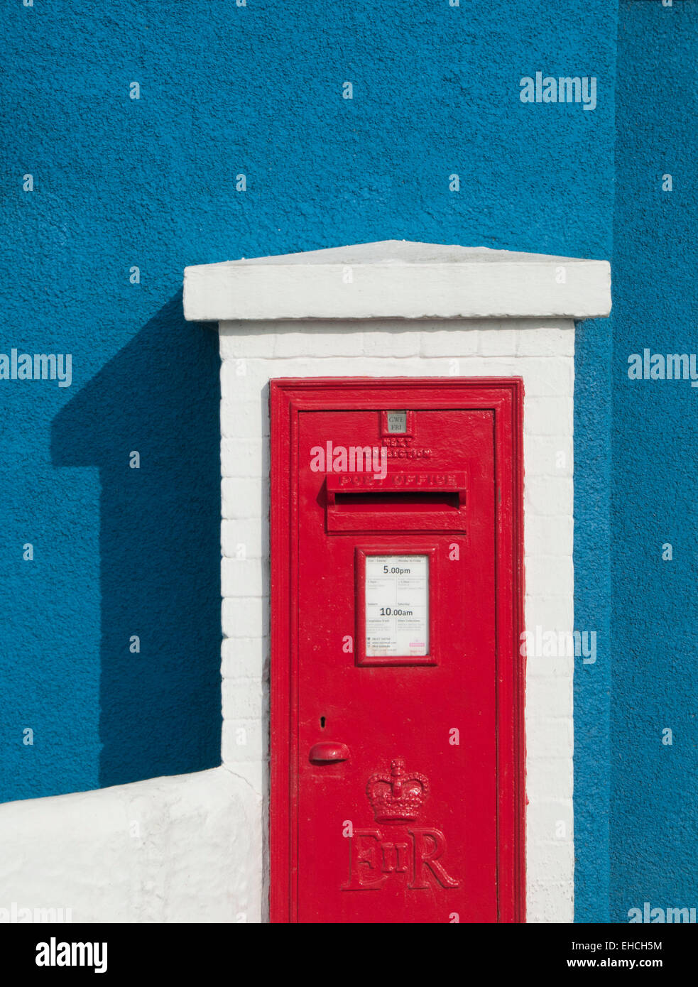 Boite aux lettres rouge vif contre un mur bleu, Llangefni, Anglesey, au nord du Pays de Galles, Royaume-Uni Banque D'Images