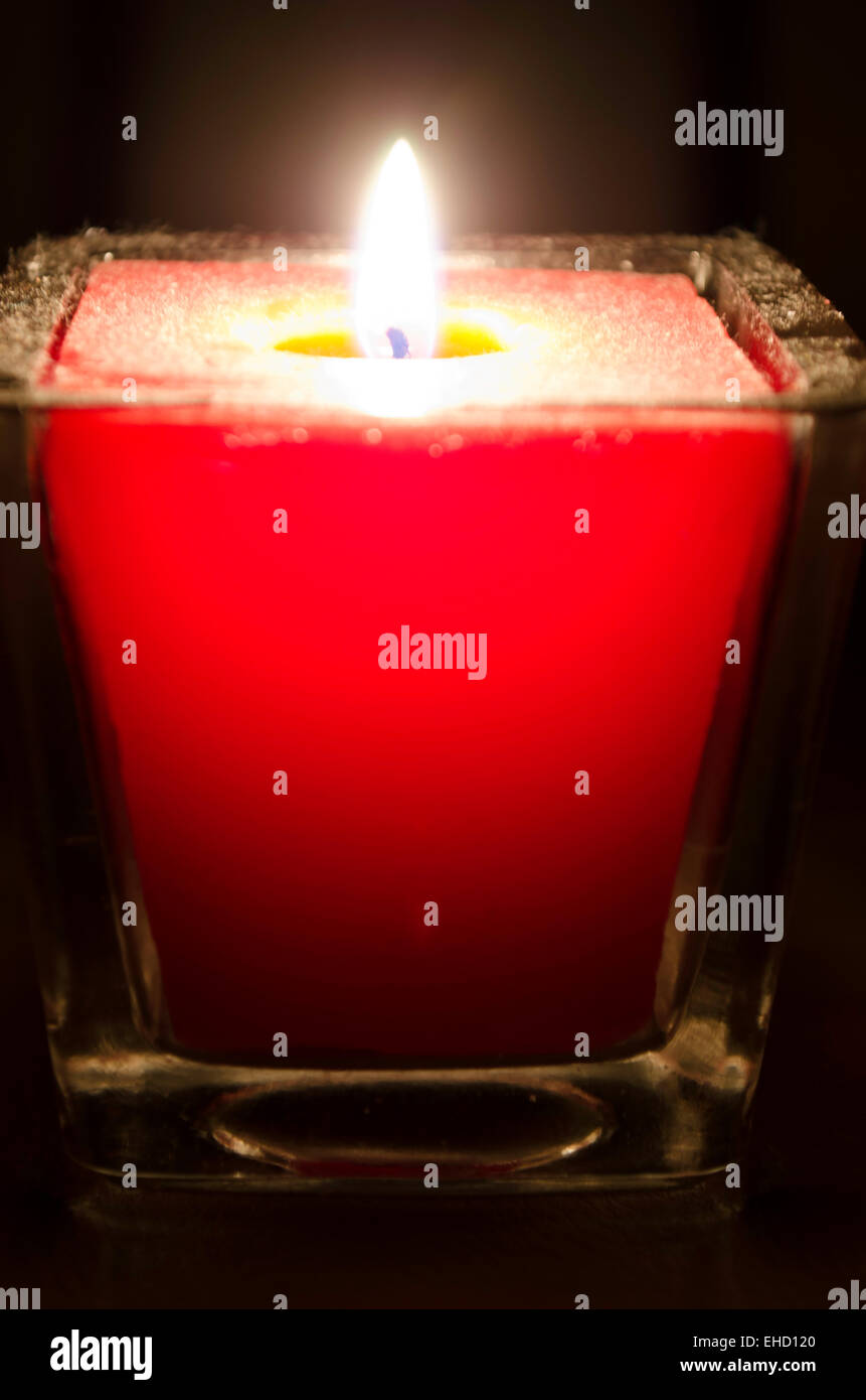 Une poussière, cire rouge, bougie de ménage burns une seule flamme jaune  vif dans une pièce sombre (fond noir Photo Stock - Alamy