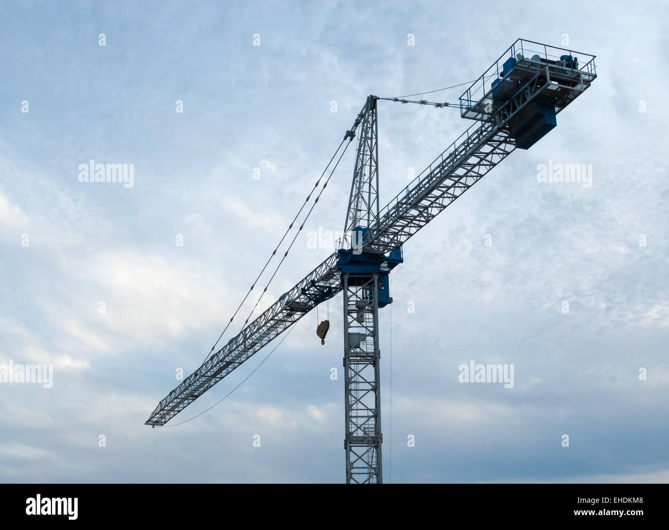 Grue de construction blanc et bleu vers la gauche contre couvert ciel gris. Banque D'Images