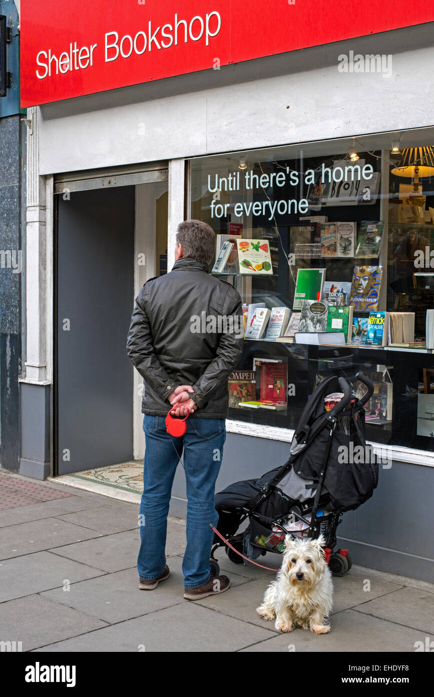Un homme avec un West Highland Terrier attend à l'extérieur un abri actions librairie , à Stockbridge, Édimbourg, Écosse, Royaume-Uni. Banque D'Images