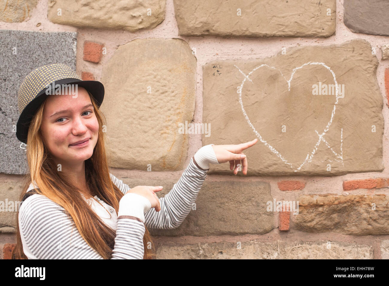 Jeune jolie fille dans le chapeau près du mur avec de la craie dessiné coeur. Banque D'Images
