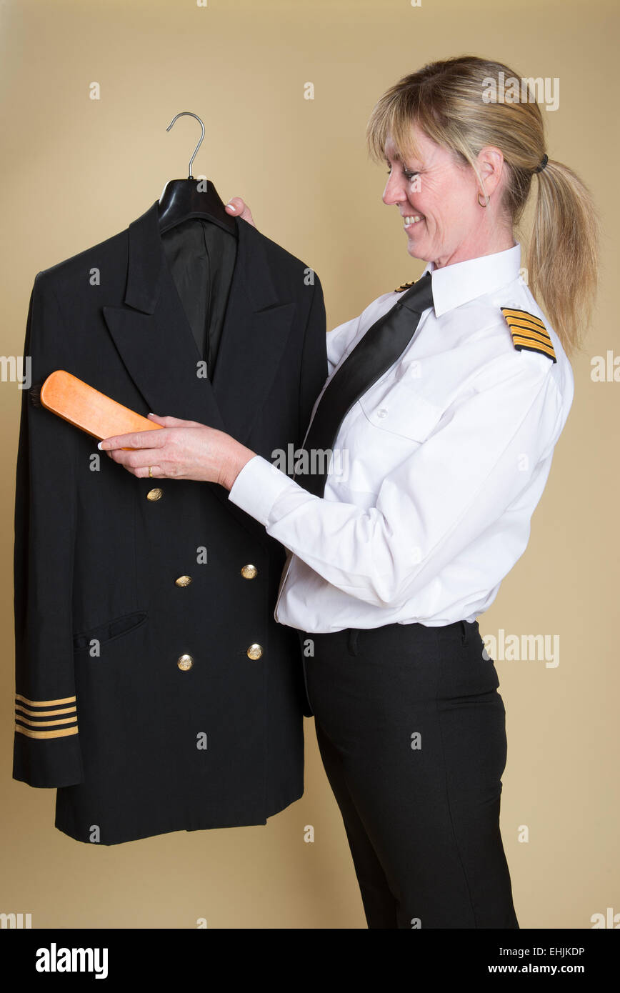 Le capitaine de la compagnie aérienne féminine la poussière de brossage son uniforme jacket Banque D'Images