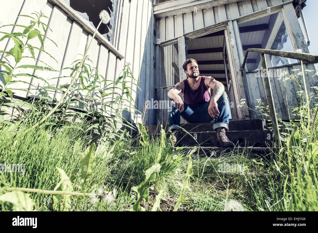 Un jeune homme assis à l'extérieur de maison abandonnée et la fumée de cigarettes. Banque D'Images